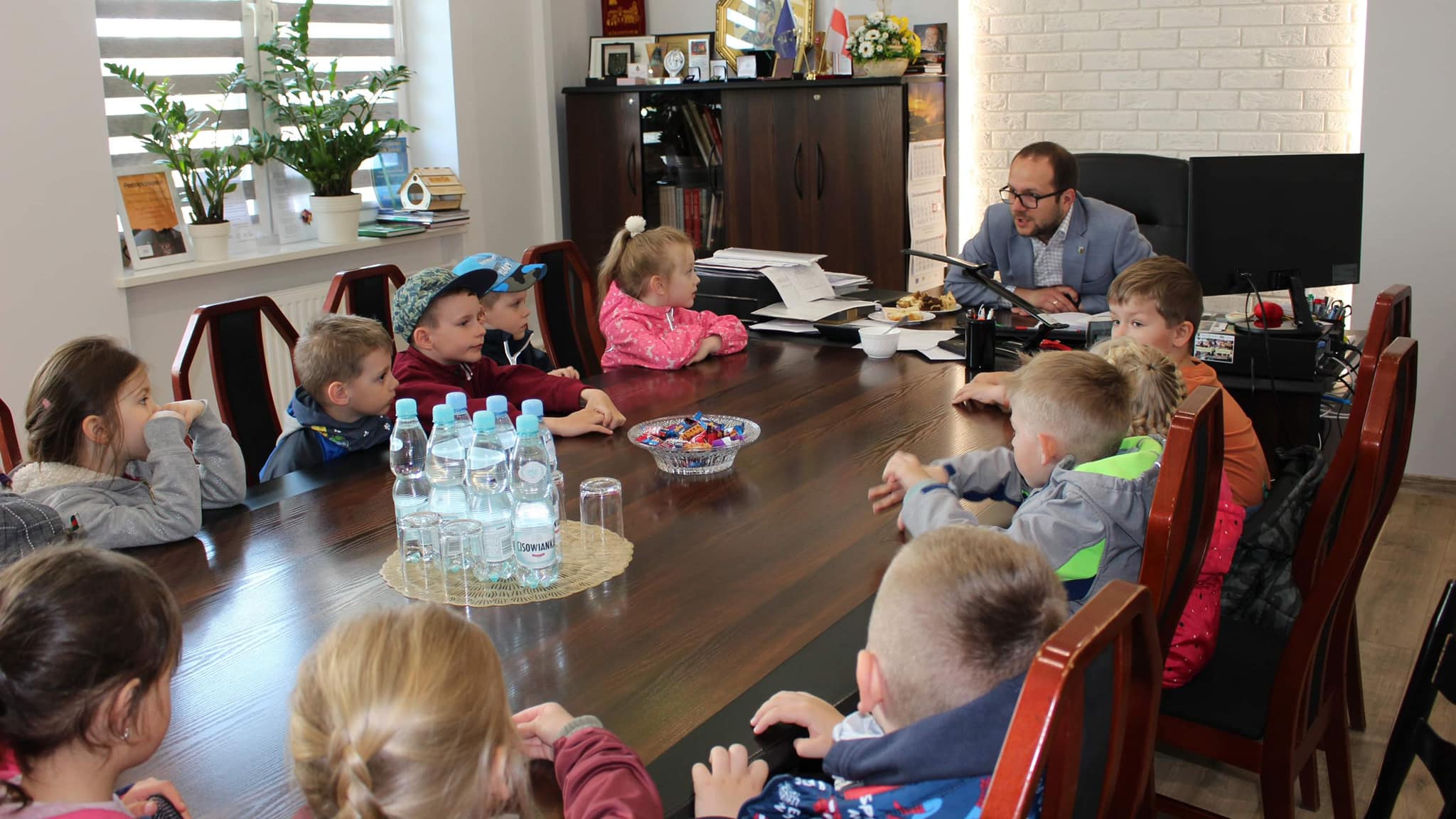 Burmistrz Dąbrowy Białostockiej w swoim gabinecie z przedszkolakami siedzącymi przy stole